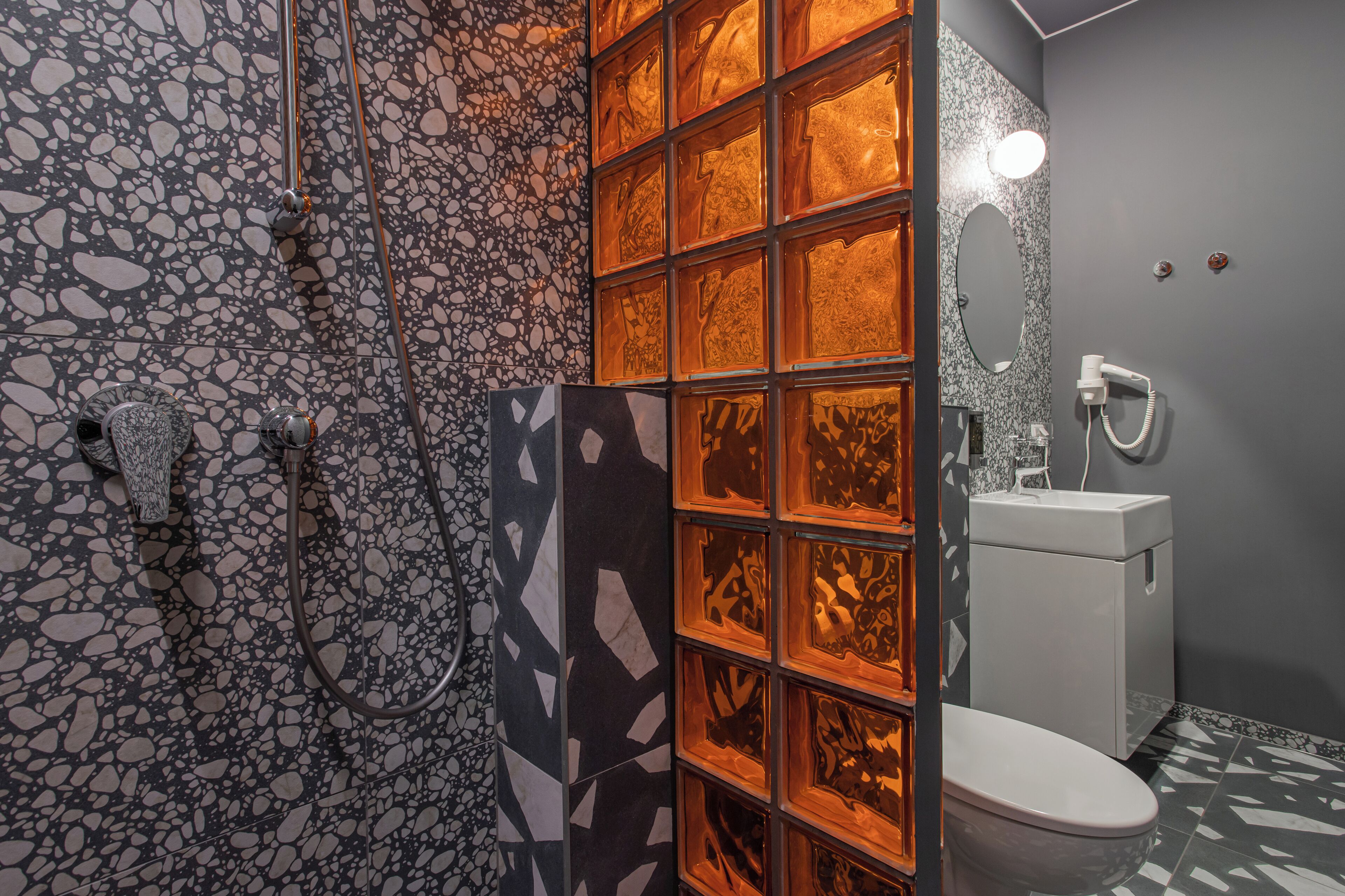 Un baño con pared de mosaicos, cabina de ducha con mampara de vidrio y un inodoro blanco.