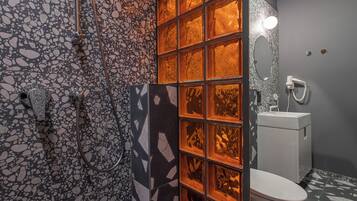A bathroom with a mosaic tile wall, a glass shower enclosure, and a white toilet.