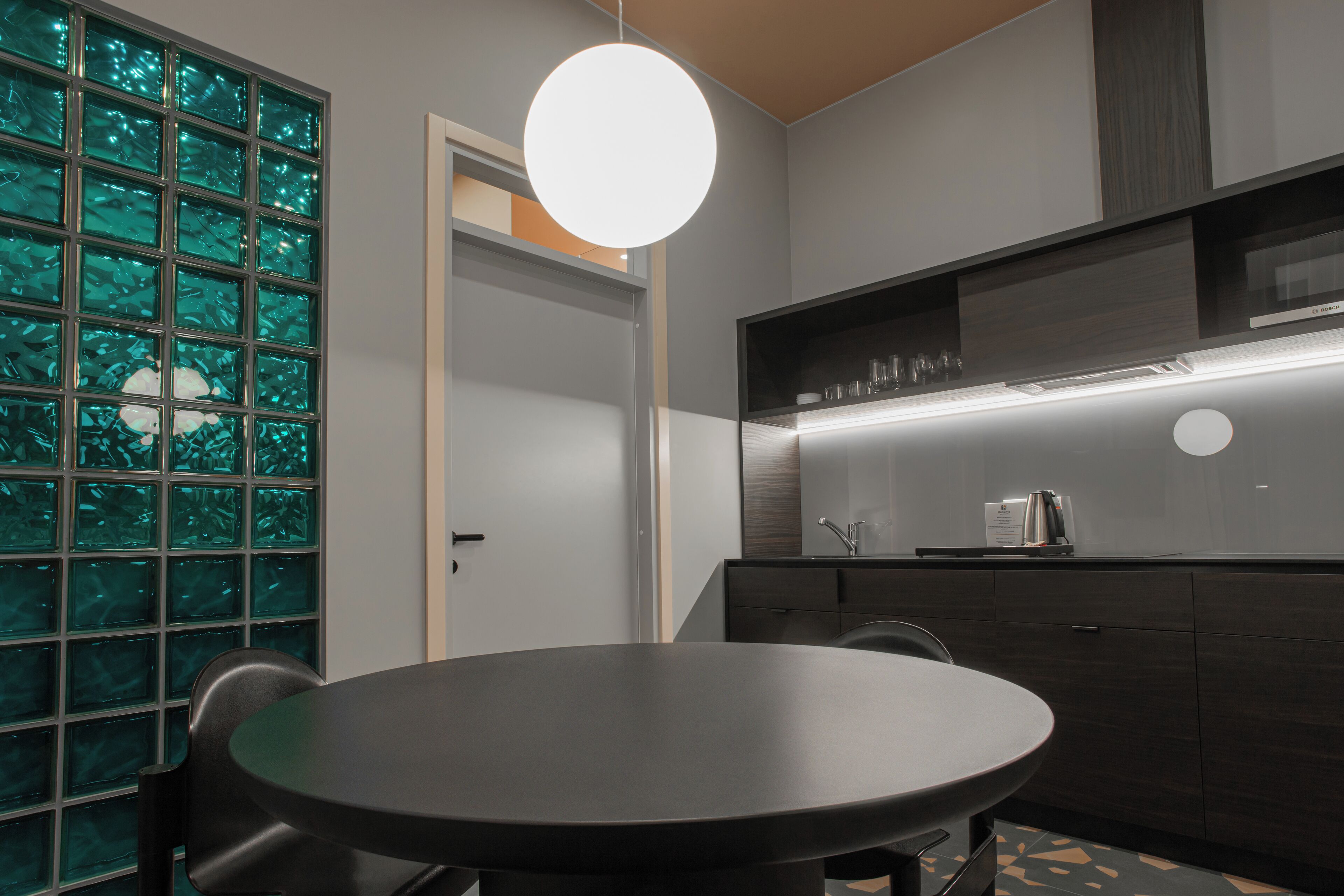 Une cuisine moderne avec une table de salle à manger ronde, des meubles de rangement aux couleurs sombres et une grande fenêtre dotée de vitres teintées en vert.