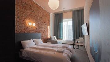 A hotel room with a brick wall, a large bed, a sofa, a TV, and a window with curtains.