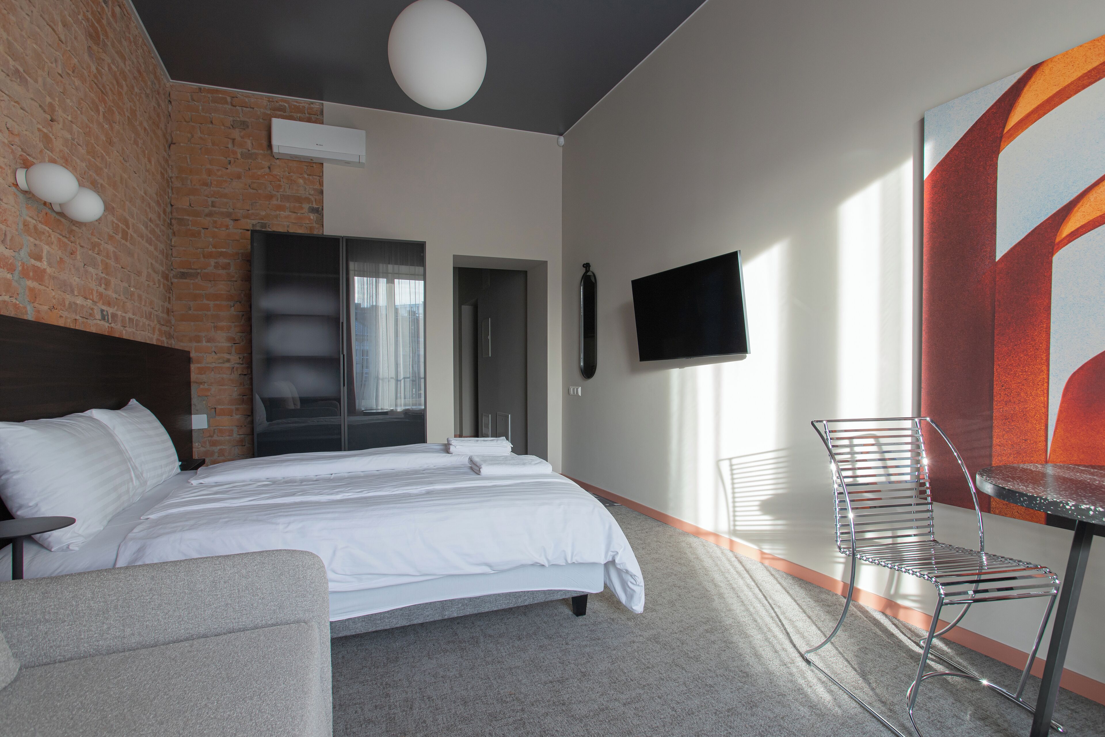Una habitación de hotel moderna con una cama grande, una zona de estar con una mesa y sillas, un televisor de pantalla plana en la pared y un cuadro abstracto de gran tamaño también en la pared.