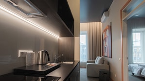 A modern hotel room with a kitchenette, a sofa, a bed, and a large window with curtains. - Resume Apartments (Kaunas)