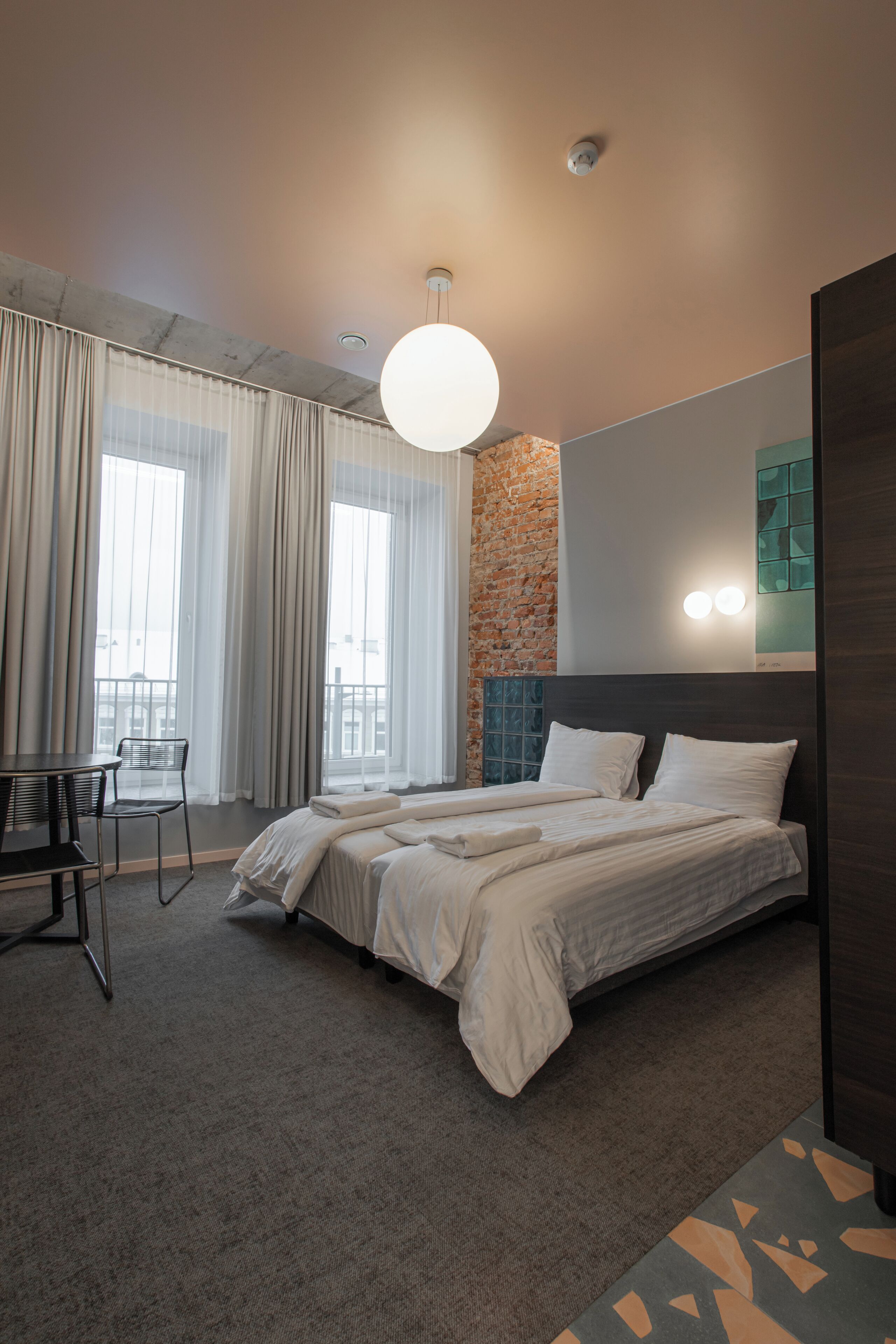 A modern hotel room with a large bed, a desk, and a view of the city through large windows.