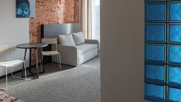 A modern hotel room with a brick wall, a grey sofa, a small table, and a large window with blue-tinted glass.