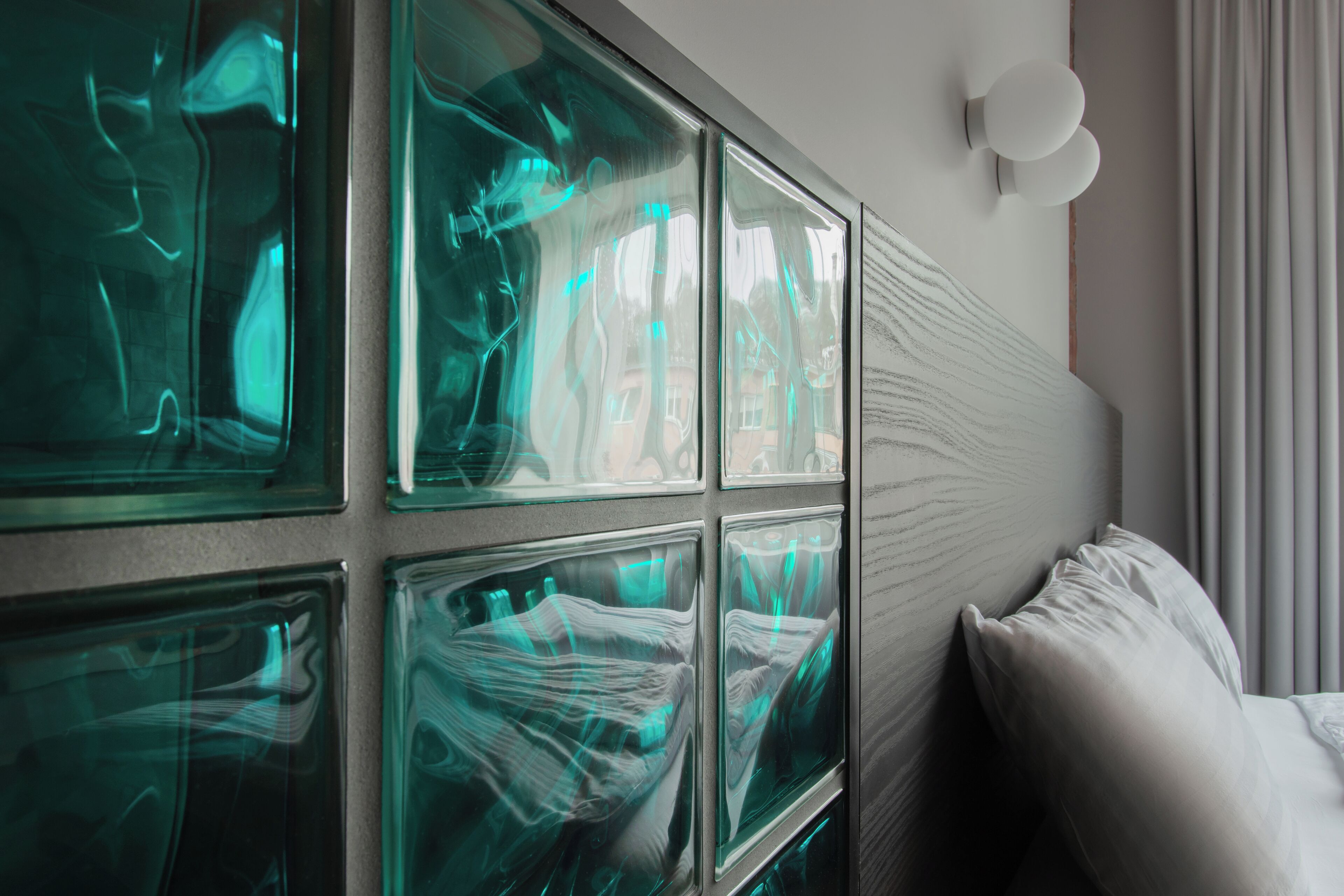 A modern hotel room with large glass windows, a bed with white linens, and a wall-mounted light fixture.