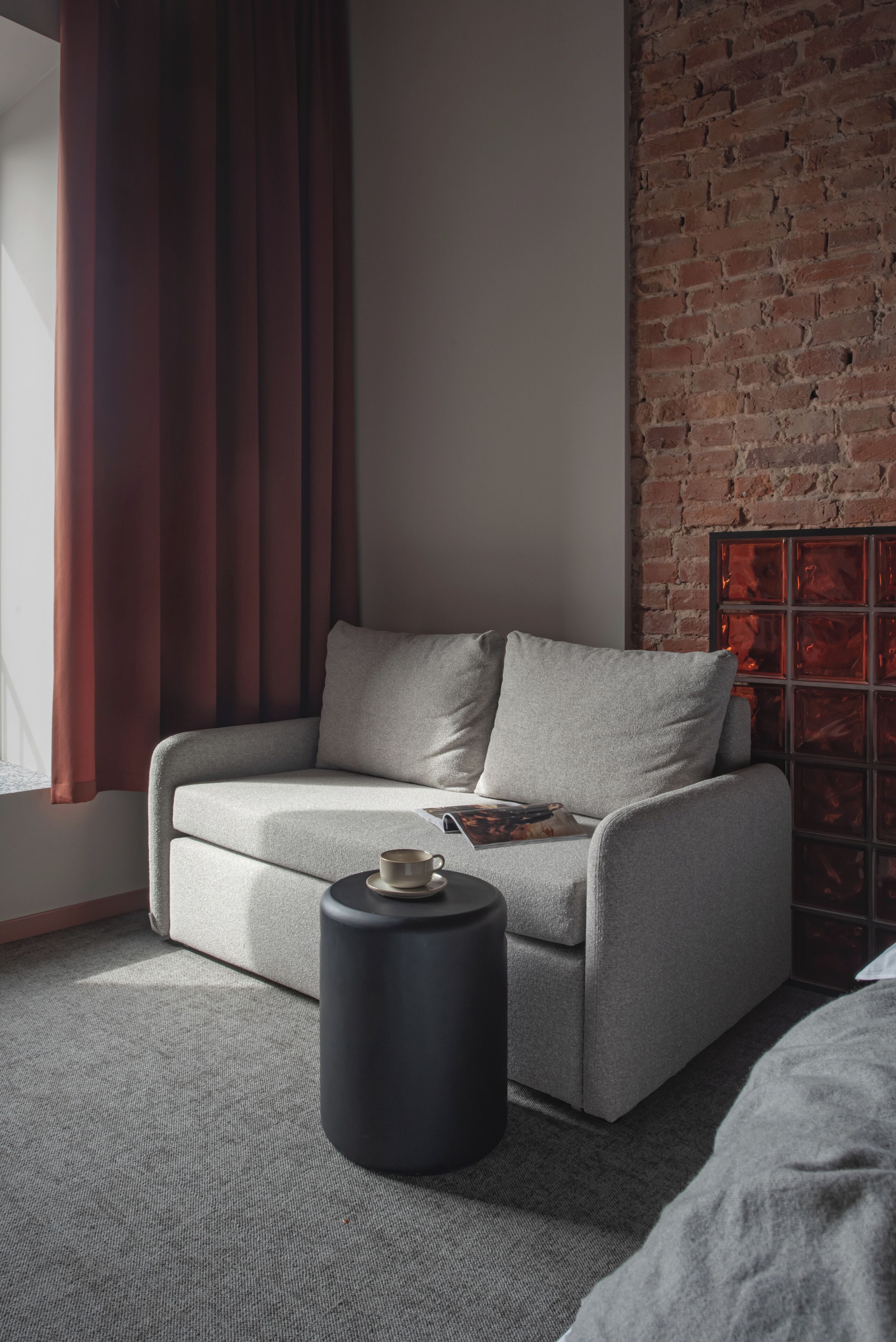 A modern living room with a grey sofa, a small black side table, and a brick wall.
