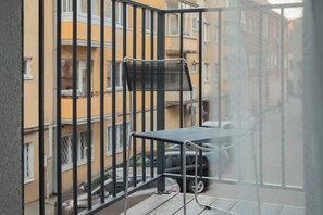 A balcony with a metal chair and a table, overlooking a street with parked cars and buildings. - Resume Apartments (Kaunas)