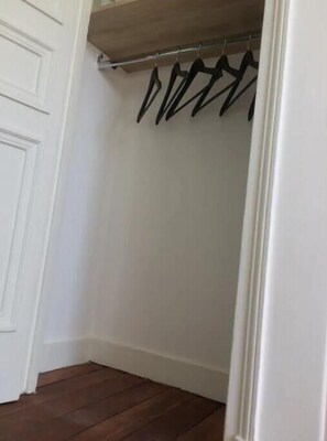 A room with a wooden floor, white walls, and a white door. There is a coat rack with several black hangers. - VUE Tour Eiffel Depuis LE Balcon Studio Lumineux Avec VUE SUR LES Toits DE Paris (Paris)