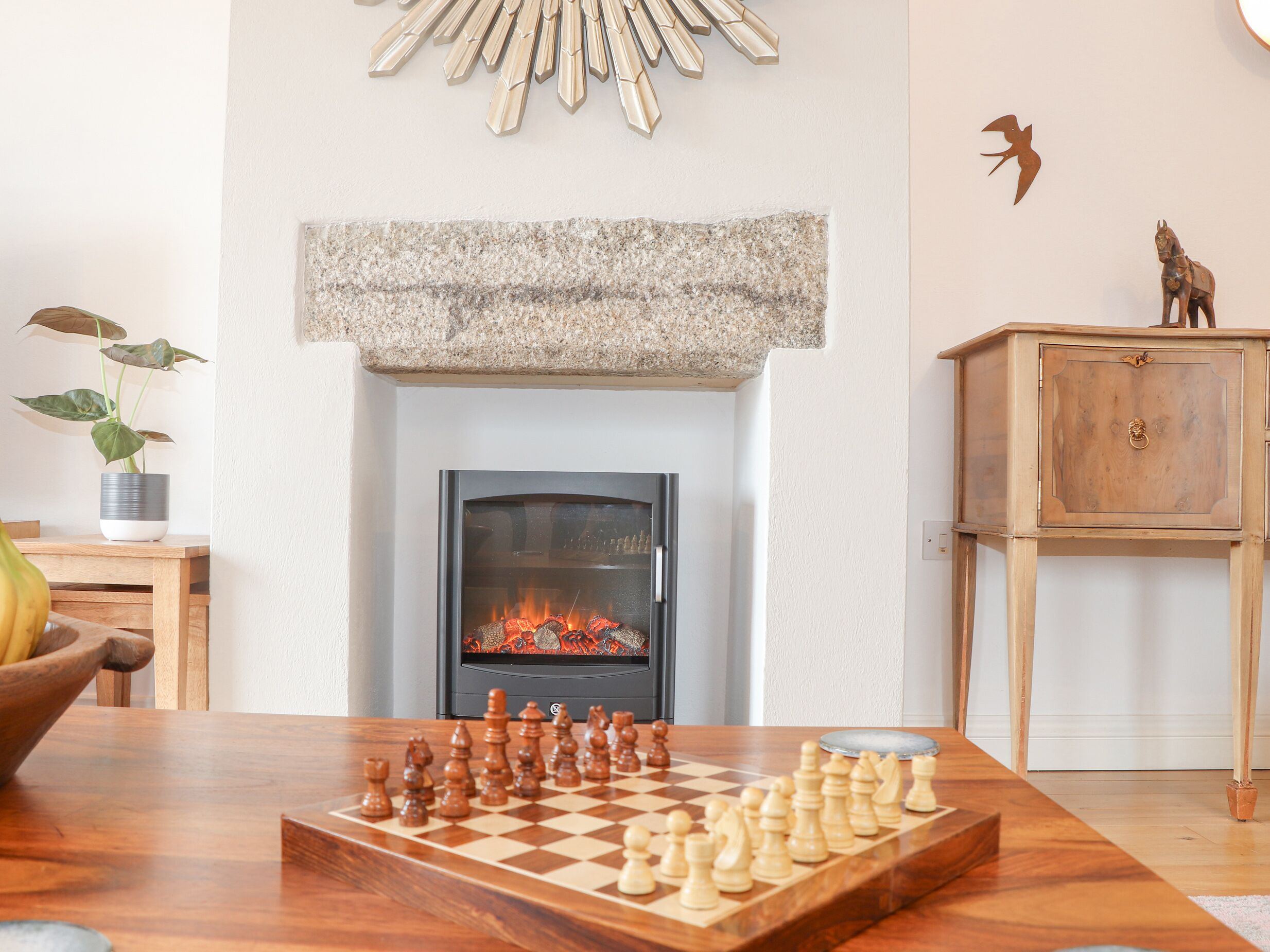 A living room with a fireplace, a chessboard, a wooden cabinet, and a plant.