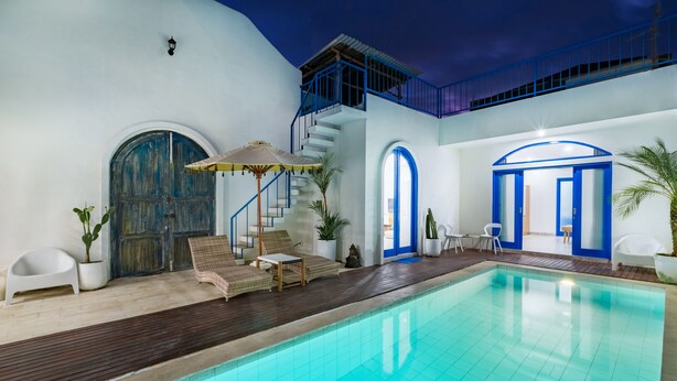 Une piscine dotée d’une terrasse en bois et de chaises longues, un escalier avec des rampes bleues et un mur extérieur blanc.