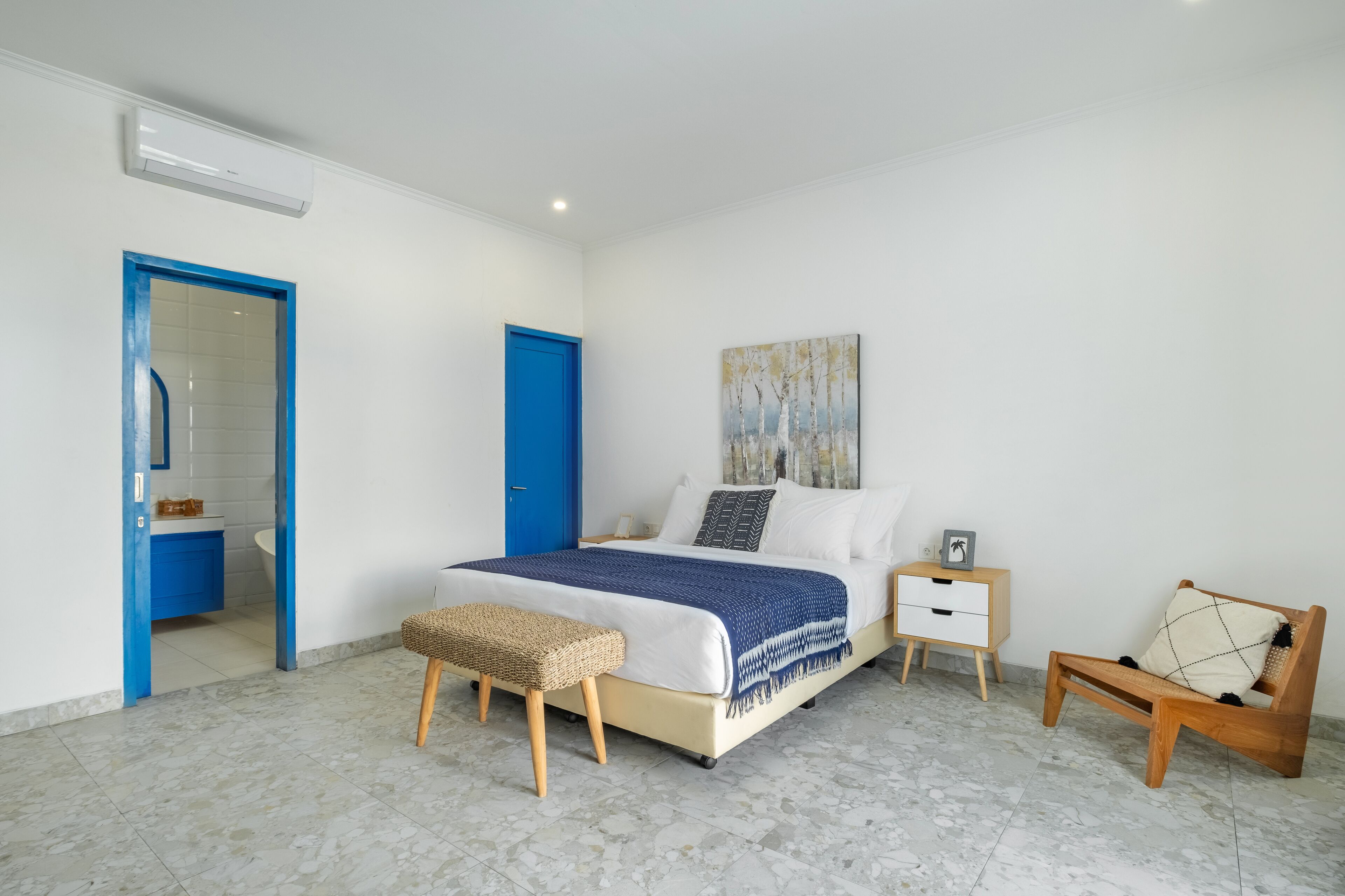 A bedroom with a bed, bedside tables, a bench, and a door leading to a bathroom.