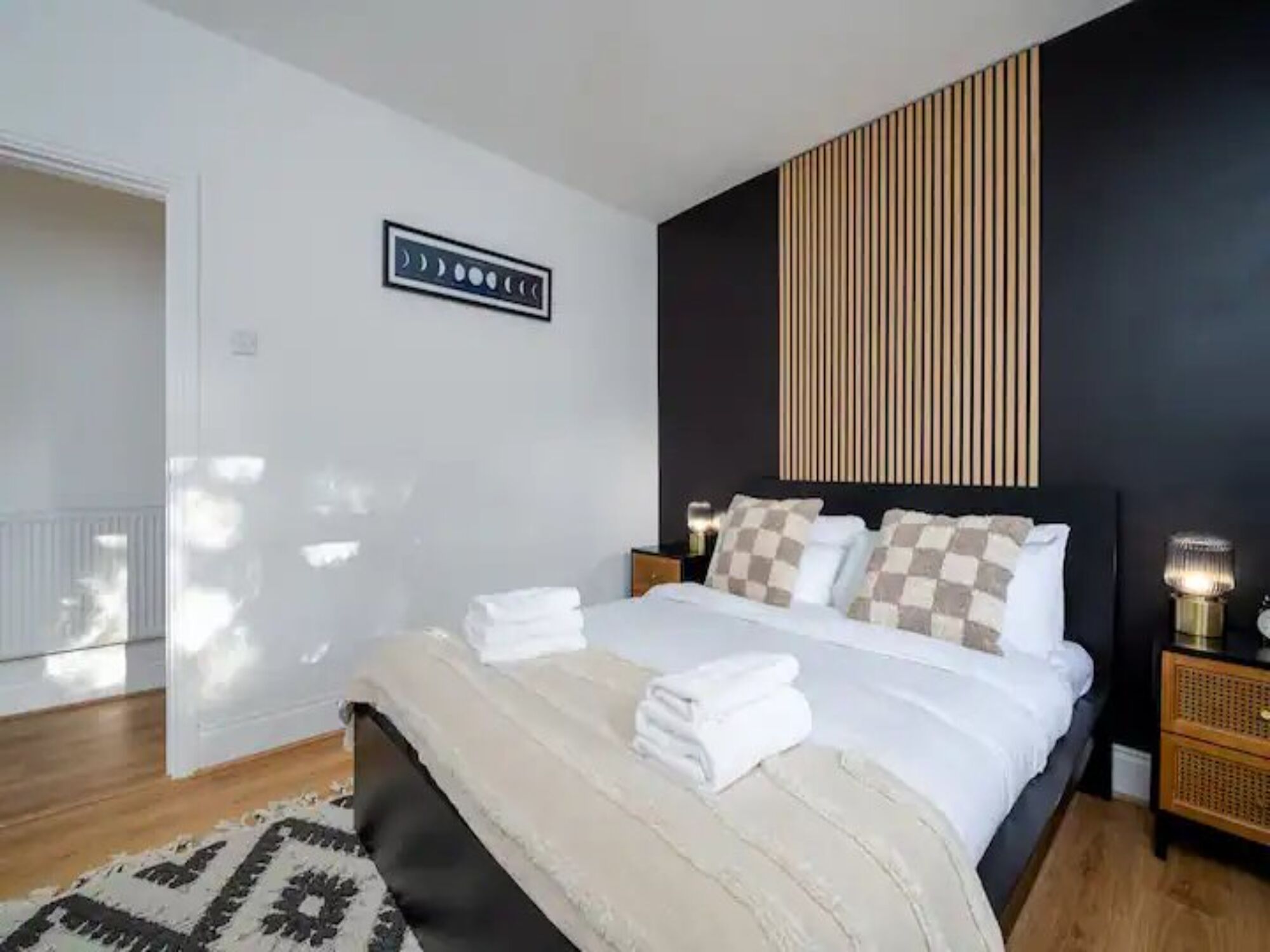 Ein modernes Schlafzimmer mit einem großen Bett, einer Wandverkleidung aus Holzleisten, einem gemusterten Teppich und einem Nachttisch mit Lampe.