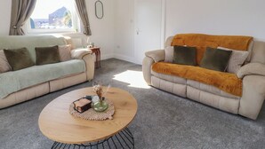A living room with two sofas, a coffee table, and a window with curtains. - Bridge End (Skipton)