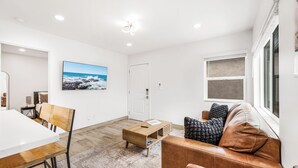 Een moderne woonkamer met een witte tafel, een houten salontafel, een bruine leren bank en een groot raam.