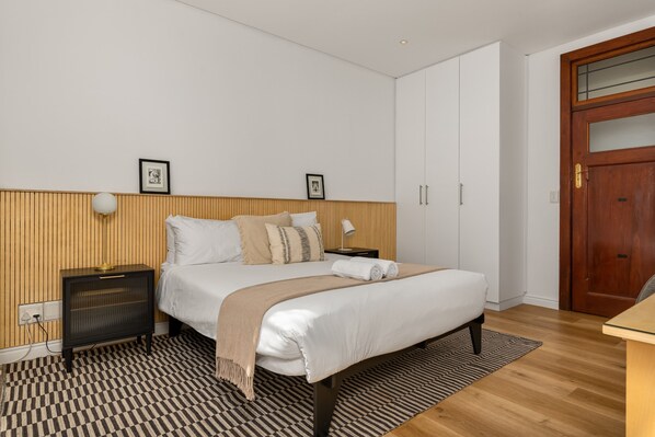 A neatly arranged bedroom with a bed, bedside tables, a wooden headboard, and a wardrobe.