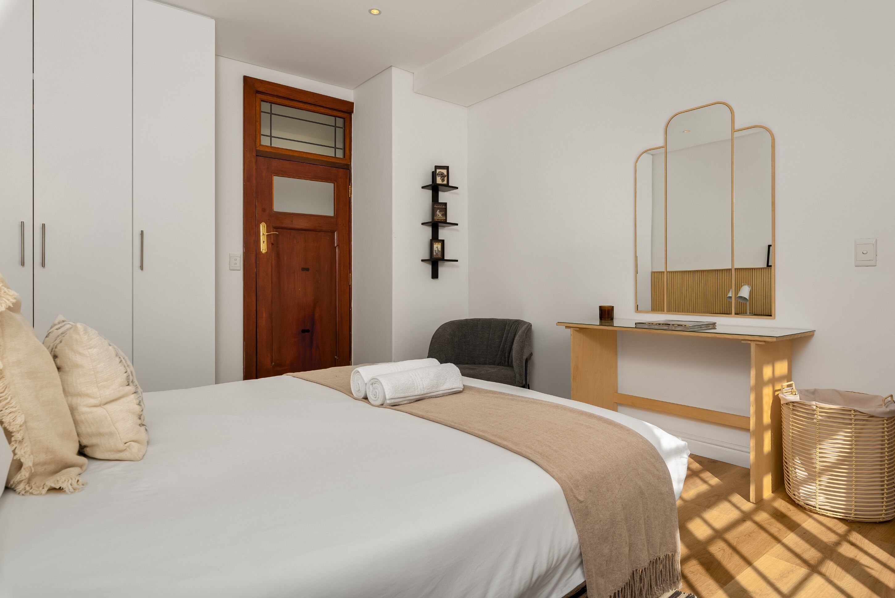 Een slaapkamer met een bed, een houten deur, een spiegel, een stoel en een tafeltje met een lamp.