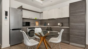 A modern kitchen with a stainless steel refrigerator, a glass-top dining table, and white chairs. - Modern 1 Bedroom Apartment in Century City (Century City)