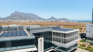 A modern building with solar panels on the roof, a glass facade, and a view of distant mountains and a cityscape. - Modern 1 Bedroom Apartment in Century City (Century City)