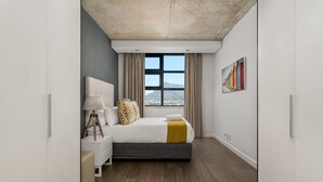 A modern bedroom with a large bed, a bedside table with a lamp, a window with curtains, and a painting on the wall. - Modern 1 Bedroom Apartment in Century City (Century City)