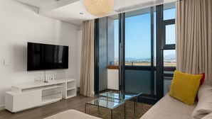 A modern living room with a flat-screen TV, a glass coffee table, and a sofa with a yellow pillow. - Modern 1 Bedroom Apartment in Century City (Century City)