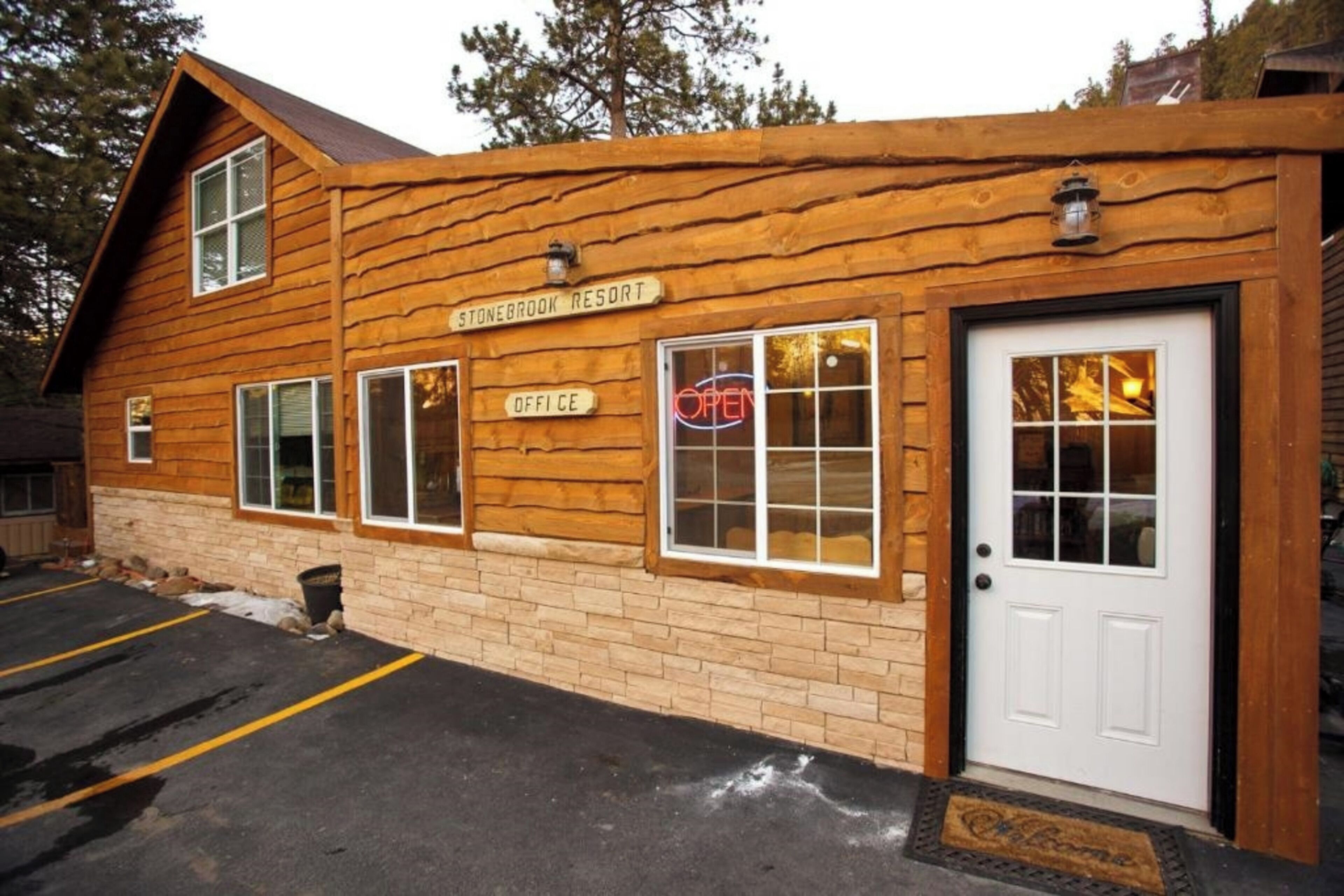 A rustic log cabin with a sign reading "Stonebrook Resort Office" and a neon "OPEN" sign.