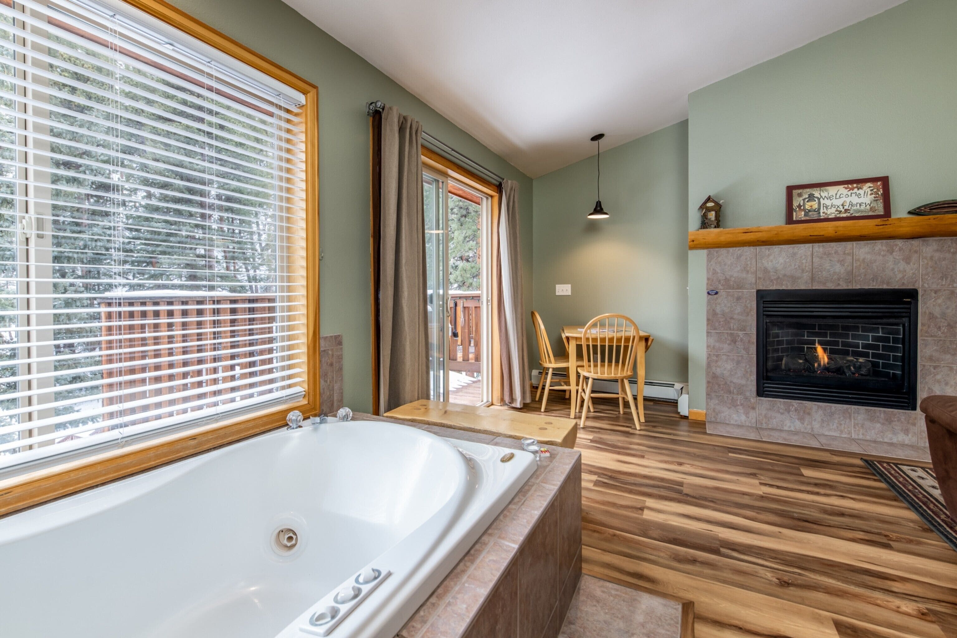 A spacious living room with a large bathtub, a fireplace, and a view through a window with blinds.
