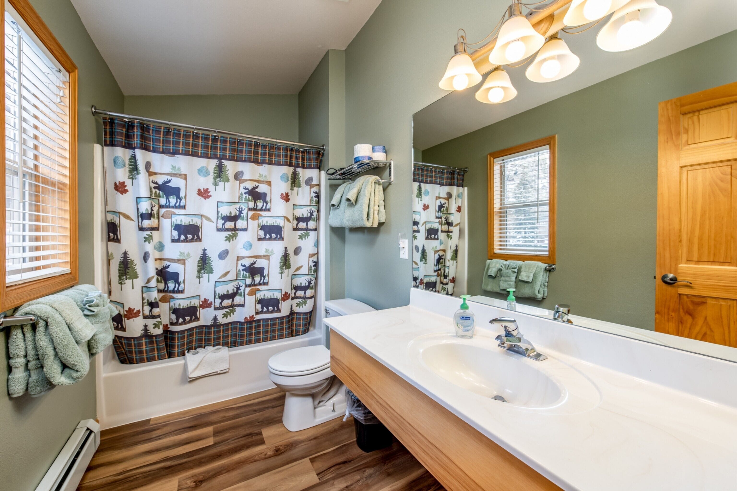 A bathroom with a large mirror, wooden vanity, and a shower curtain with a nature print.