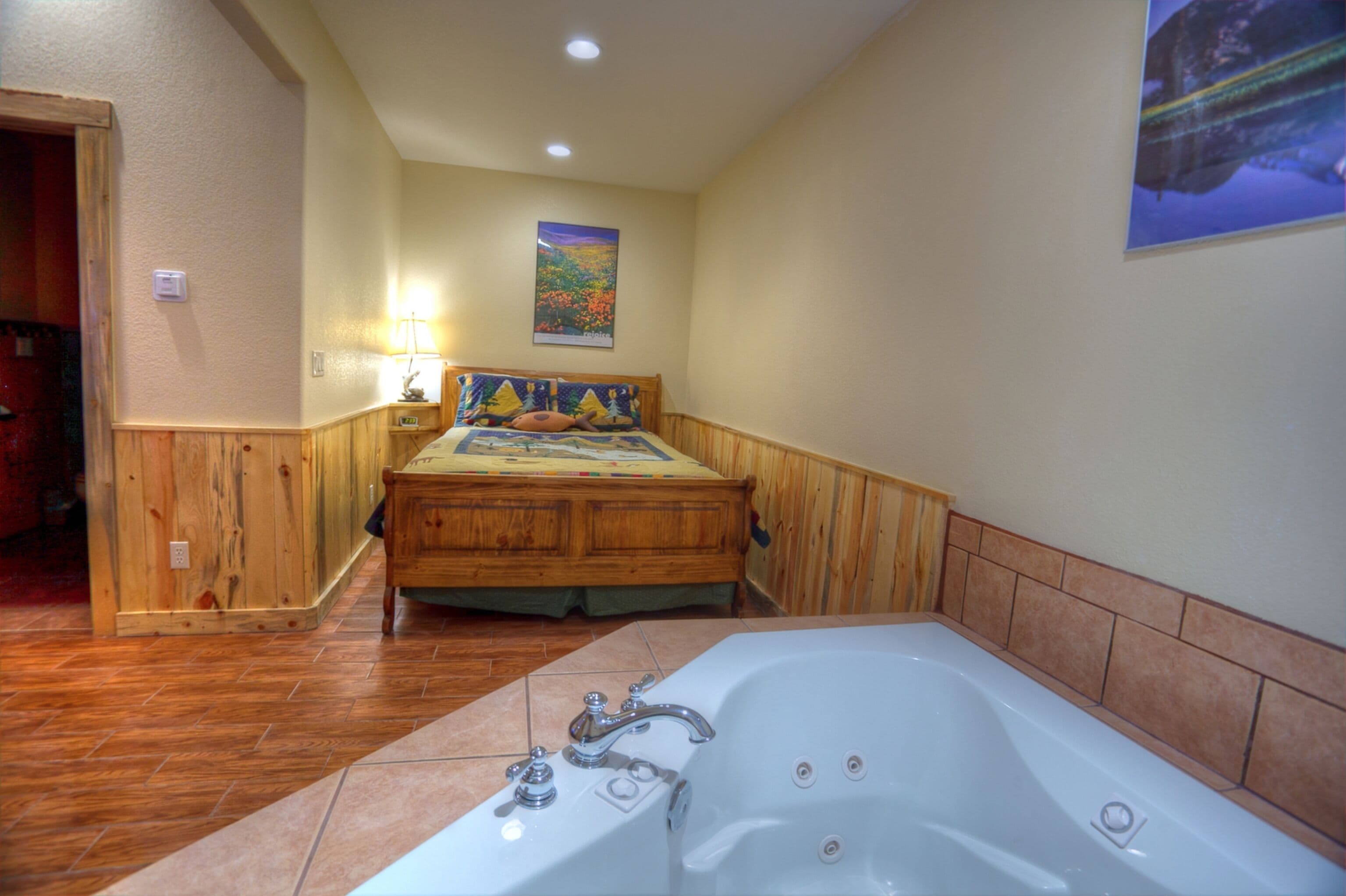 A bedroom with a wooden bed, a large bathtub, and a painting on the wall.