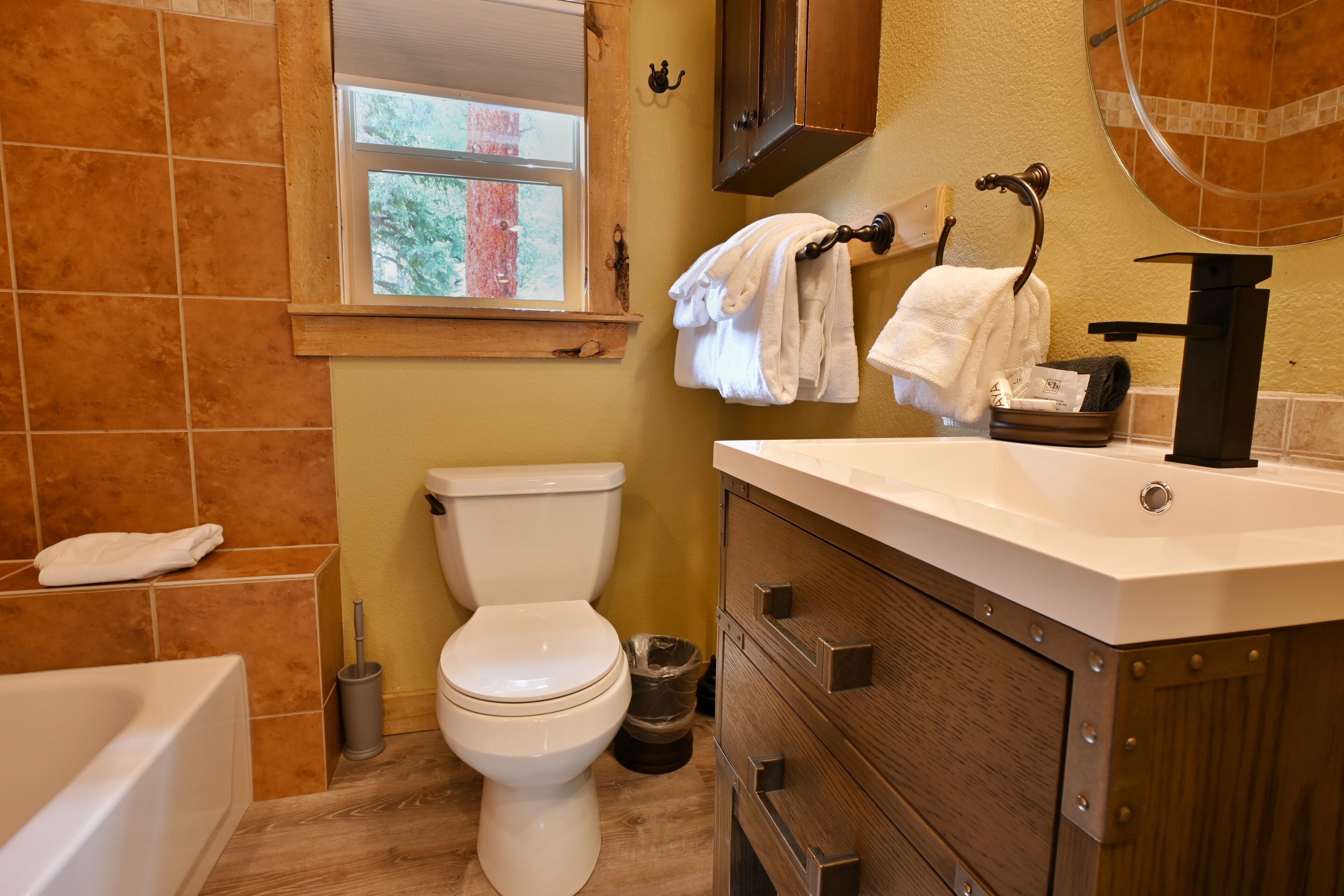 A bathroom with a toilet, sink, and bathtub. There is a window above the toilet, and towels are hanging on a rack.