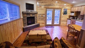 Interior de una cabaña de madera con chimenea de piedra, muebles de madera y una zona de cocina.