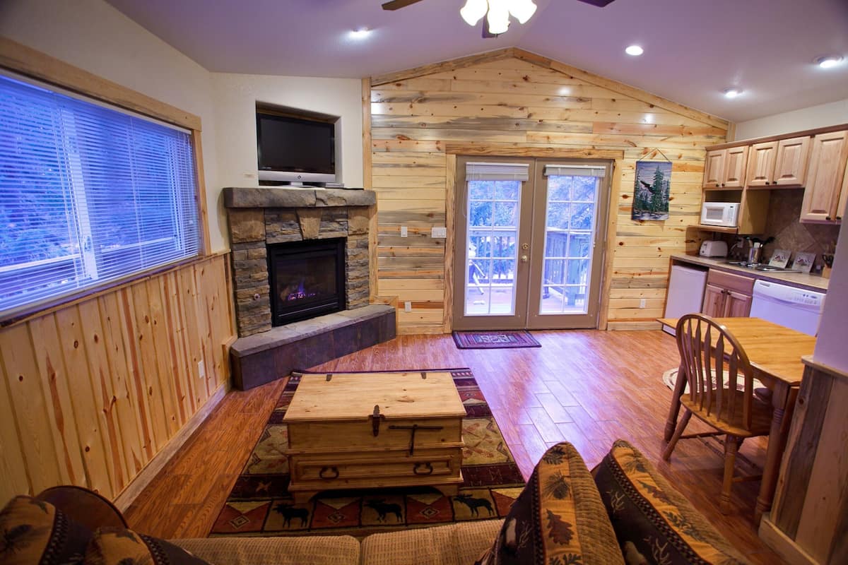 L’intérieur d’une cabane en rondins, avec une cheminée en pierre, des meubles en bois et un coin cuisine.
