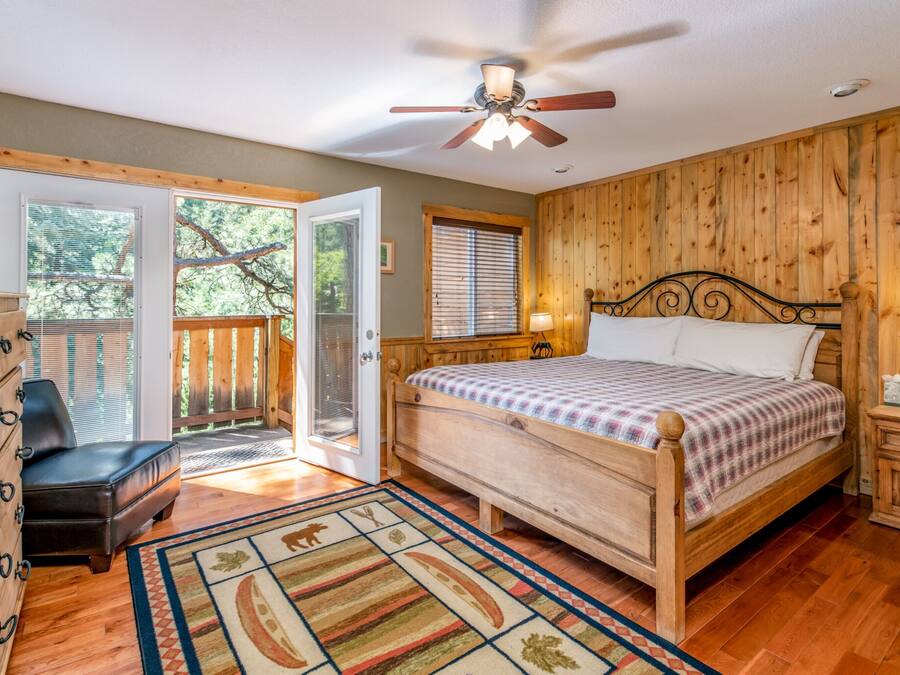 A bedroom with a wooden bed, a ceiling fan, a nightstand, a dresser, and a view of the outdoors through a sliding glass door.