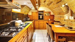 A kitchen with wooden cabinets, a gas stove, and a stone wall. - The Old Wine Cellar - 4 bedroom property (Oakerthorpe)