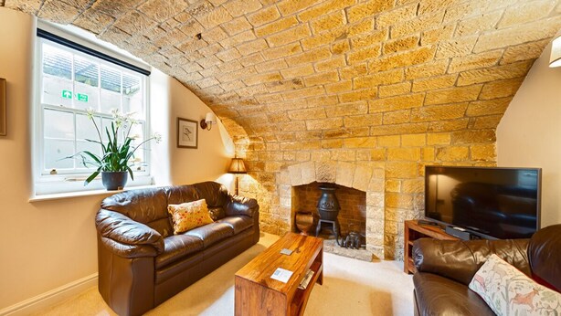 A cozy living room with a stone fireplace, leather sofas, a wooden coffee table, and a flat-screen TV. - The Old Wine Cellar - 4 bedroom property (Oakerthorpe)