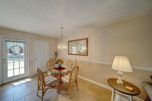 Un coin repas avec une table ronde, des chaises en osier, un lustre, un miroir et une lampe.