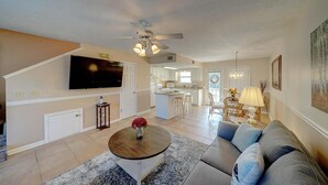 A spacious living area with a large TV, a ceiling fan, and a kitchen in the background. - 206 White Sandy-pet Friendly (Panama City Beach)