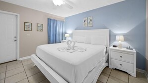 Un dormitorio con cama, mesita de noche, ventilador de techo y decoración en la pared.