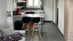 A modern kitchen with a dining area, grey walls, and a grey sofa with a colorful pillow.