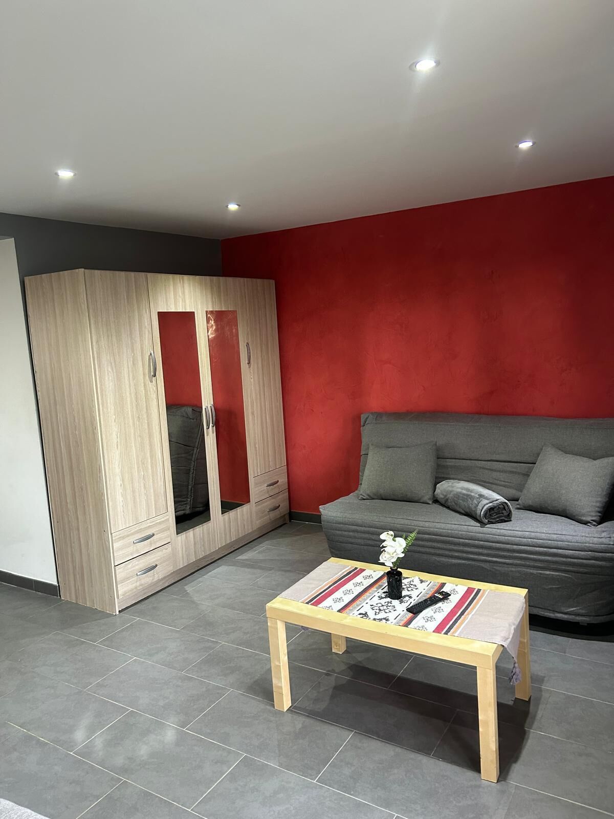 A modern living room with a grey sofa, a wooden wardrobe, and a small wooden coffee table.