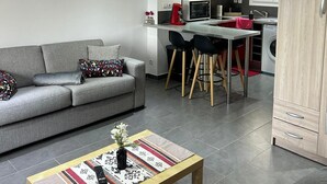 A modern living room with a grey sofa, a coffee table with a vase, and a kitchen area with red cabinets and a microwave.