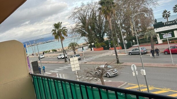 A view from a balcony overlooking a busy street with palm trees, cars, and a building with a sign that reads "France".