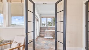 A hallway leading to a bathroom with a tiled floor, a bench, and a view of the outside. - 20816 Front Beach Rd (Panama City Beach)