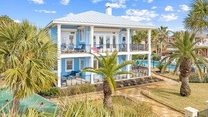 A two-story house with a pool, surrounded by palm trees and a clear blue sky. - 20816 Front Beach Rd (Panama City Beach)