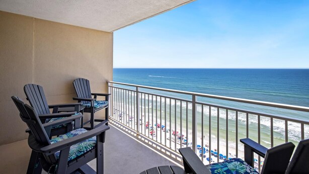 A balcony with two Adirondack chairs, a small table, and a view of the ocean and beach. - Emerald Beach 1430 (Panama City Beach)
