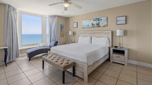 A hotel room with a large bed, a bench, a desk, and a view of the sea. - Emerald Beach 1430 (Panama City Beach)