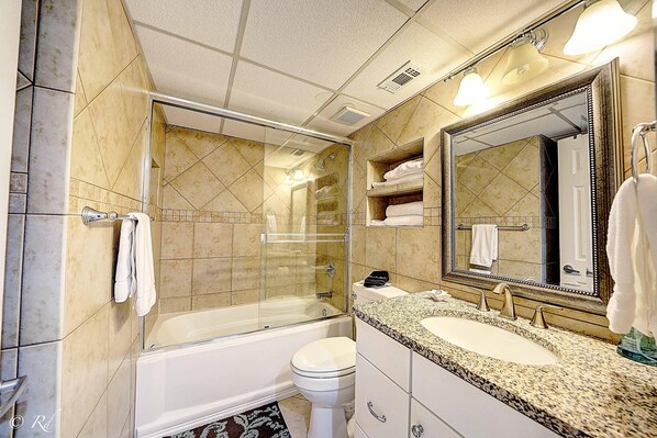 Une salle de bain dotée d’une douche à parois de verre, de toilettes blanches, d’un lavabo avec un plan de travail en granit et d’un grand miroir.