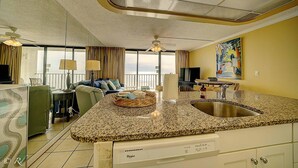 A kitchen with a granite countertop, a built-in dishwasher, and a large window overlooking the ocean. - Edgewater 1008-3 (Panama City Beach)