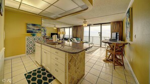A spacious kitchen with a large island, a dining area with a table and chairs, and a balcony with a view. - Edgewater 1008-3 (Panama City Beach)