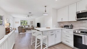 Une cuisine moderne avec des meubles blancs, un four encastré et un four à micro-ondes. On y trouve également un coin repas avec un canapé et des chaises.