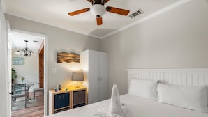 A hotel room with a bed, a ceiling fan, a wardrobe, a desk with a lamp, and a dining area with a table and chairs. - 7904 Surf Dr #7 (Panama City Beach)